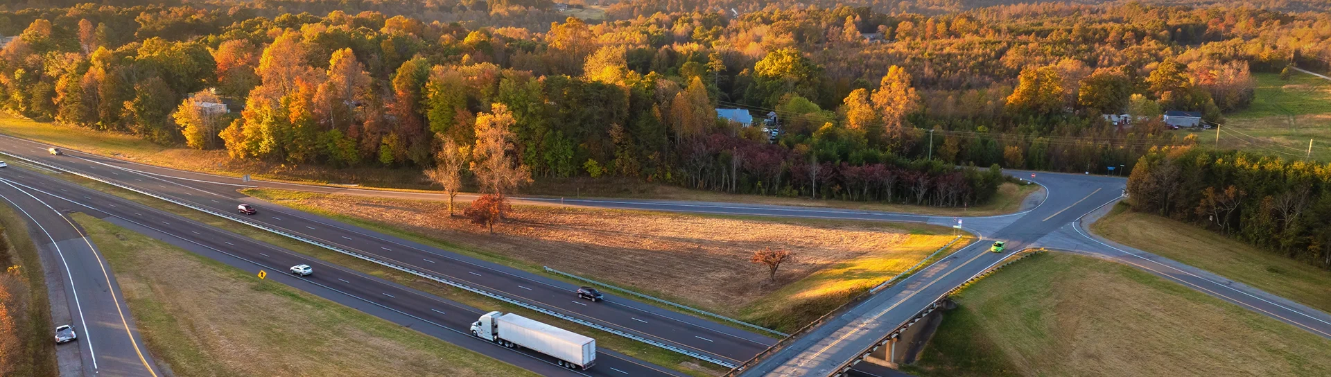 Aerial view of a highway intersection surrounded by trees with autumn foliage and light traffic including cars and a semi-truck